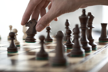 Wooden chess board during game on chessboard. Playing wooden chess pieces. Successful business strategies, leadership in any endeavor. Player's hand moves the black knight. Wooden chess set carved
