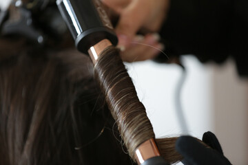 Fixing a woman's beautiful, blonde hair with a black curling iron.