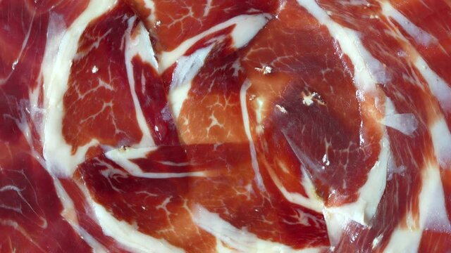 Thin slices of Iberian ham from pigs fed with acorns on a rotating plate. Tasty typical sausage from Spain