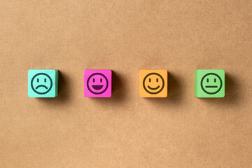 Emoticon faces in colors wooden blocks over brown paper. Service evaluation and satisfaction survey concepts. Angry, neutral, good mood and happy. Copy space. Flat lay photo.