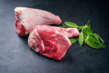 Raw traditional lamb shank with herbs offered as close-up on a black board with copy space