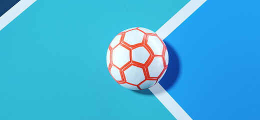 Close-up of a white orange futsal ball in the corner of a bright blue soccer field background