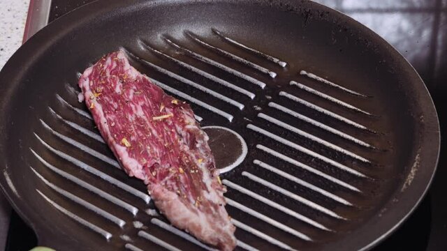 Raw wagyu meat gold label 9+ top view, cooking on a pan. Hand puts steak premium cut flap variety with spices on hot fryer.
