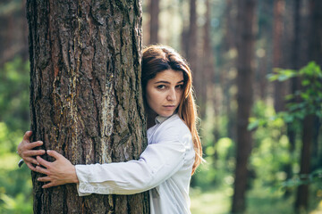 Young beautiful female volunteer hugs a tree with love in the forest