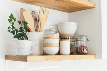 Kitchen shelves with various white ceramic and glass jars. Open shelves in the kitchen. Kitchen interior open shelving ideas. Eco friendly kitchen, zero waste home concept