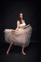 Fototapeta na wymiar Young girl in white top and peach skirt dancing in black old textured studio