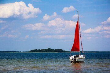 Little sailing boat with a red sail on a big lake