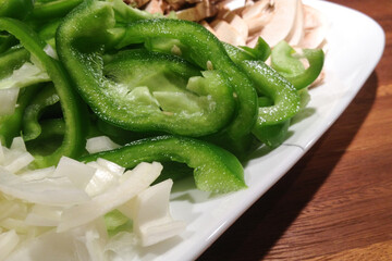 Close Up of Plate of Raw Vegetables with Green Bell Peppers, Onions, and Mushrooms