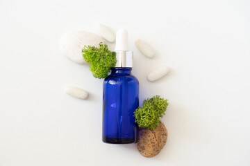 Sea moss personal care. Blue bottle with oil dropper and sea stones and moss on white background....