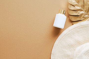 Suntan cream container mockup, straw beach hat, golden monstera leaf on sandy background. Flat lay, top view, copy space.