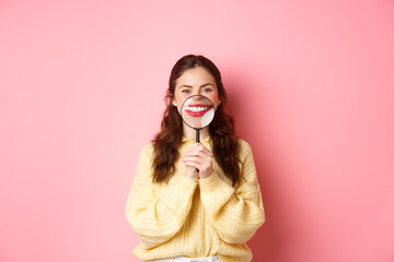 Stomagology and healthcare concept. Young beautiful girl with perfect smile, showing her white teeth with magnifying glass, standing against pink background - obrazy, fototapety, plakaty