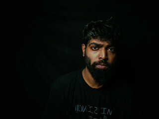 Fototapeta premium Indian bearded man with facial hair and expressions for social media posts and web banners with black background wearing a black tshirt studio shot of indian male model with piercing 