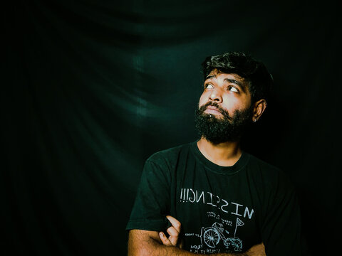 Indian bearded man with facial hair and expressions for social media posts and web banners with black background wearing a black tshirt studio shot of indian male model with piercing
