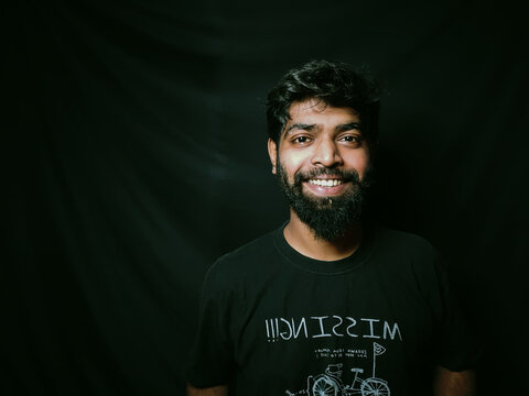 Indian bearded man with facial hair and expressions for social media posts and web banners with black background wearing a black tshirt studio shot of indian male model with piercing
