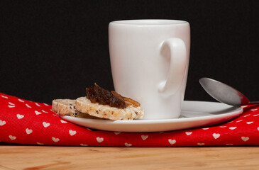  a cup of coffe beside a spoon and a rice vegan cookies with a jelly on the top