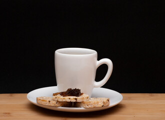 cup of coffe beside a rice vegan cookies with jelly on the top under the wood table