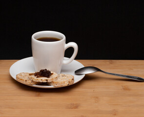 cup of coffe beside a rice vegan cookies with jelly on the top and spoon under the wood table