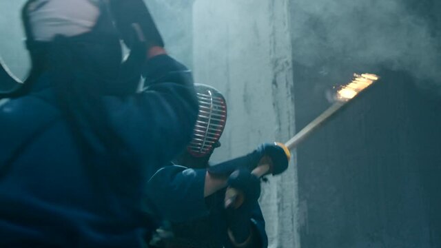 Japanese kendo fighters with burning swords competing in the fog in dark mystic industrial building . Super mystical video . Battle of two kendo fighter with fire sword . Shot on ARRI Alexa Camera .