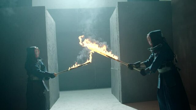Japanese kendo fighters with burning swords competing in the fog in dark mystic industrial building . Super mystical video . Battle of two kendo fighter with fire sword . Shot on ARRI Alexa Camera .