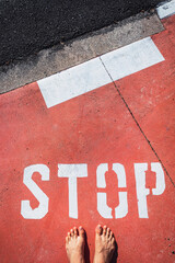 An illegal immigrant stands barefoot at a stop sign on the ground.