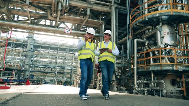 Male colleagues are walking along the premises of the refinery plant