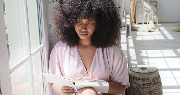 A young mixed-race lady is attentively reading an intriguing book, a fiction, a novel, while pondering about what he was reading. A peaceful day at home without the use of technological devices or