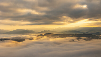 Fototapeta na wymiar Sun rays through the clouds and beautiful mist in the mountains in wonderful morning sunrise natural landscape.