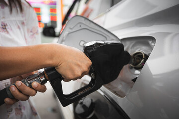 Close up on woman hand holding fuel nozzle and put in to automobiles tank to filling diesel gas fuel at gas station.