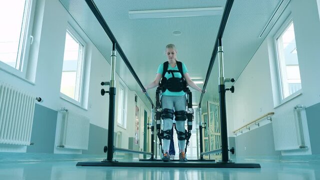 Handicapped woman is walking in the exosuit with medical aid.