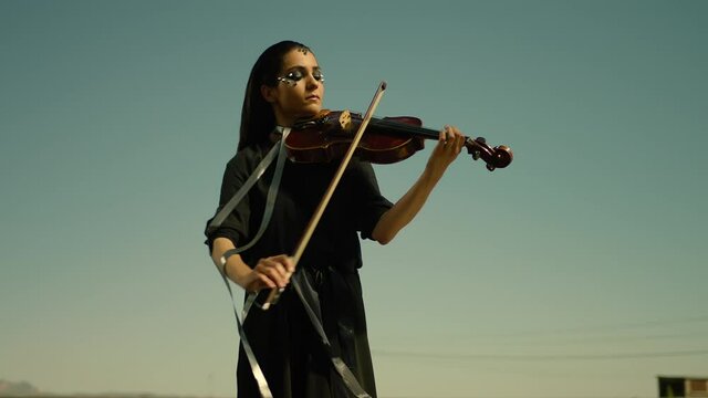 Black dressed young girl playing the violoncello on roof of the building . Alone female musician plays the violin . Woman plays violin . Outdoor shot on ARRI ALEXA Cinema Camera in slow motion .