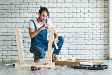 Hipster young man working as handyman, assembling wood table with equipments and manual, concept...