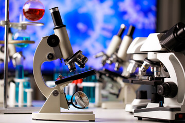 Scientific microscope with lens objectives on chemistry experiment table in microbiology lab with apparatus for physical substance research and study to enhance human healthiness against disease