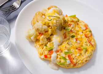 Delicious vegetable omelette served on white plate with cauliflowers, grated cheese and cream sauce..