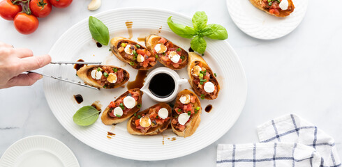 Top down view of a platter of homemade bruschetta with a hand using tongs to take one from the platter.