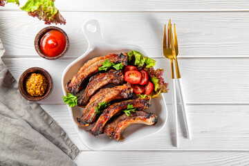  Baked pork ribs with vegetables, mustard and ketchup on white wooden background top view vertical photo