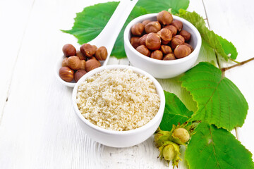 Flour and hazelnuts in bowls on white wooden board