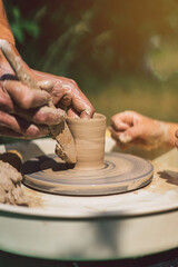 Potter making a clay object on pottery wheel in outdoors. Craftsman moulding clay with hands on pottery wheel