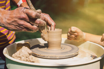 Potter making a clay object on pottery wheel in outdoors. Craftsman moulding clay with hands on pottery wheel