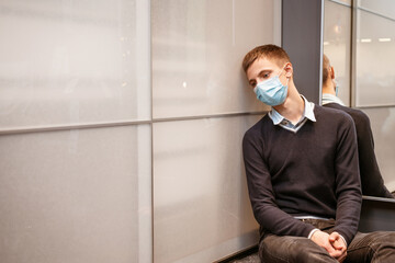 a guy of Caucasian nationality sits in a corner wearing a protective mask sad at the mirror.