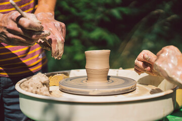 Potter making a clay object on pottery wheel in outdoors. Craftsman moulding clay with hands on pottery wheel