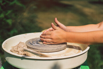 Potter making a clay object on pottery wheel in outdoors. Craftsman moulding clay with hands on pottery wheel