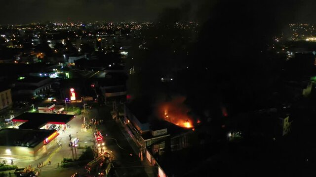 Aerial view around a warehouse on fire, in middle of a city with night lights - orbit, drone shot