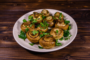Plate with baked champignons, dill and parsley on a wooden table