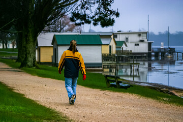 Lady wearing blue jeans, blue and yellow jacket, scarf and red gloves walking along gravel track...