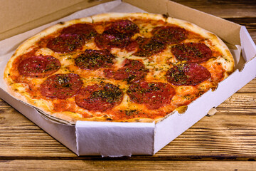 Pizza with salami sausage and parmesan cheese in cardboard box on a wooden table
