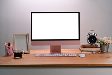 Modern workspace with computer, books, photo frame and coffee cup on wooden desk.