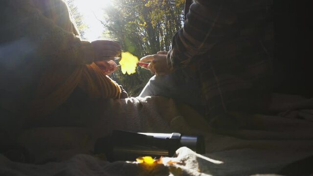 Couple sit in open trunk of hatchback car on road in autumn forest drinking hot tea from thermo cup and using smartphone for route planning. Detail shot with unrecognizable persons