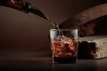 Whiskey is poured from a bottle into a frozen glass with natural ice.