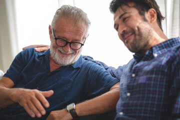 caucasian senior father and adult son are hugging together at home, generation family are happy...