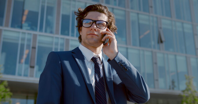 Medium shot of confident businessman in glasses talking on mobile phone outside